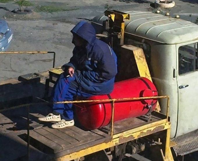 man smoking a cigarette on top of a gas cylinder, unsafe working conditions, fail