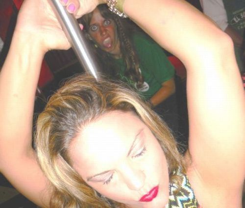 girl dancing on pole with friend photobombing her in the background, funny face