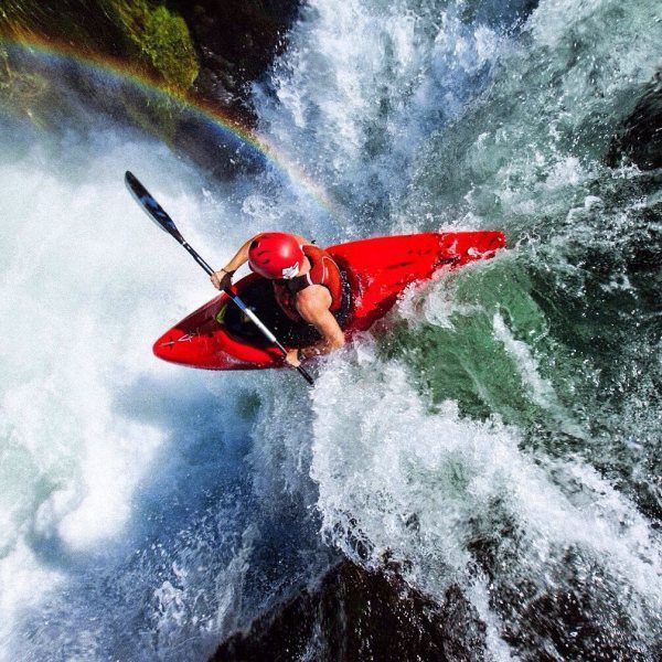 amazing photograph of kayaker going off water fall with a rainbow in the background