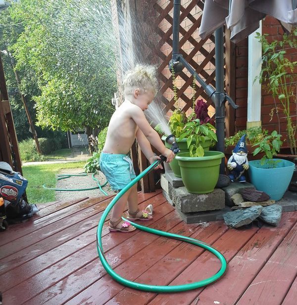kid sprays self in face while trying to water plants with hose