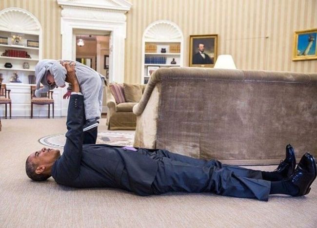 president barack obama lying on the ground playing with a costumed baby