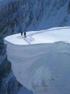 two people standing on top of a huge snow ledge