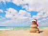 sandman, a snowman made our of sand on a tropical beach, wearing a santa claus hat