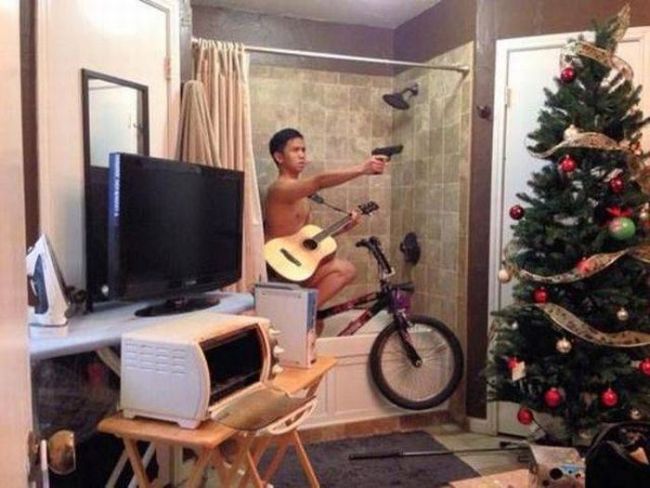 wtf photo of the day, make guy with gun and guitar on bike in bathtub next to tv microwave and christmas tree