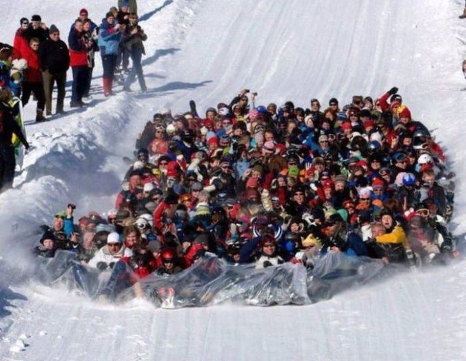 crowd of people slide down mountain on plastic sheet