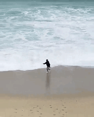 just a hop skip and wet phone away, man runs away from wave on beach only to drop his phone in the water