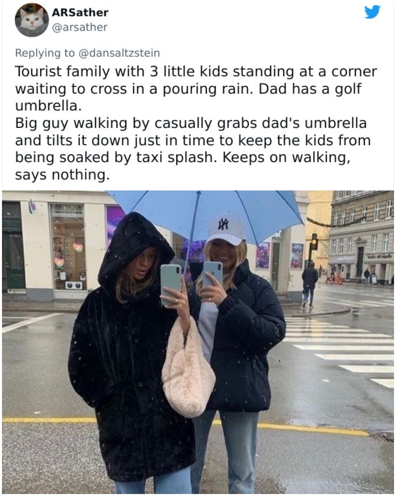 tourist family with 3 little kids standing at a corner waiting to cross in the rain, dad has a golf umbrella, big guy casually grabs dad's umbrella and tilts it down just in time to keep the kids from being soaked by a taxi splash